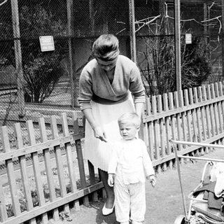 Mother and young child stand near a fence.