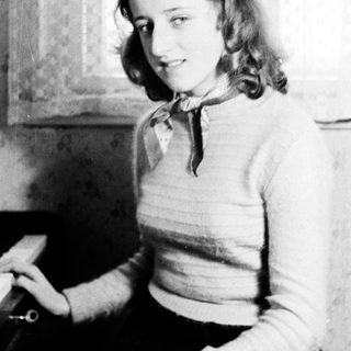Here's a brief summary of the image: Young woman sits indoors, wearing a sweater and a scarf.