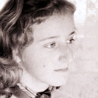 Here's a brief summary of the image: Young woman sits, looking off to the side, wearing a sweater.