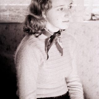 Here's a brief summary of the image: Young woman sits, looking off to the side, wearing a sweater.