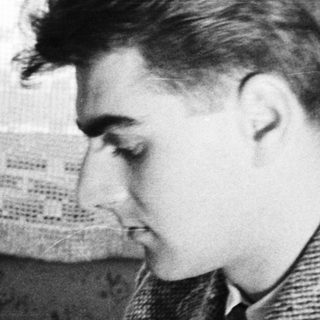 Young man in a coat, seated near a piano.
