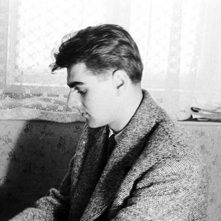 Young man in a coat, seated near a piano.