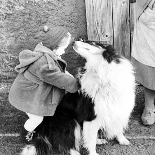 Child hugging a dog near a weathered wooden door.