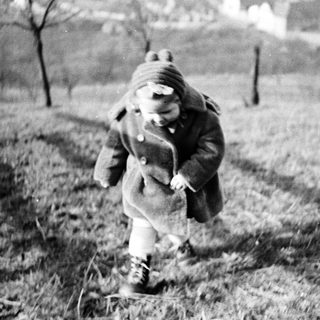 A child runs across a grassy field in a coat.