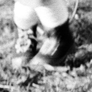 Here's a brief summary of the image: Child runs through a grassy field wearing a coat.
