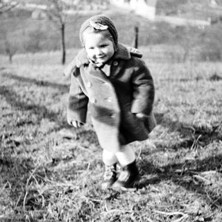 Here's a brief summary of the image: Child runs through a grassy field wearing a coat.