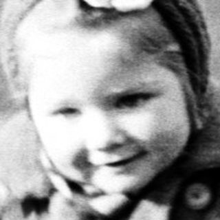 Here's a brief summary of the image: Child runs through a grassy field wearing a coat.