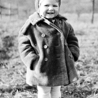 Here's a brief summary of the image: Young child in a coat stands in a field.