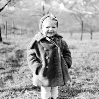 Here's a brief summary of the image: Young child in a coat stands in a field.