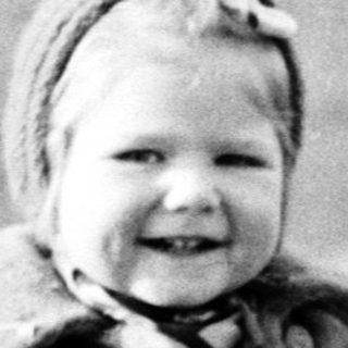 Here's a brief summary of the image: Young child in a coat stands in a field.