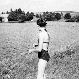 A person in a bikini stands by a lake.