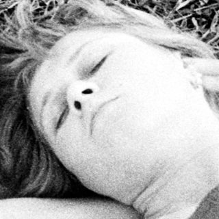 Here's a brief summary of the image: Two people sleeping together on a blanket in grass.