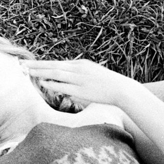 Here's a brief summary of the image: Two people sleeping together on a blanket in grass.