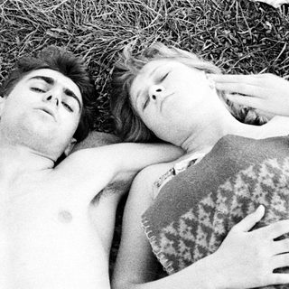 Here's a brief summary of the image: Two people sleeping together on a blanket in grass.