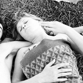 Here's a brief summary of the image: Two people sleeping together on a blanket in grass.