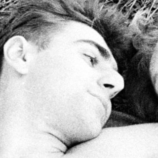 Here's a brief summary of the image: Couple lies close together on a blanket outdoors.