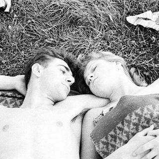Here's a brief summary of the image: Couple lies close together on a blanket outdoors.