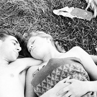 Here's a brief summary of the image: Couple lies close together on a blanket outdoors.
