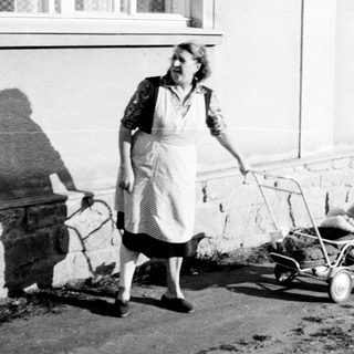 Woman walks along a path, pushing a small cart.