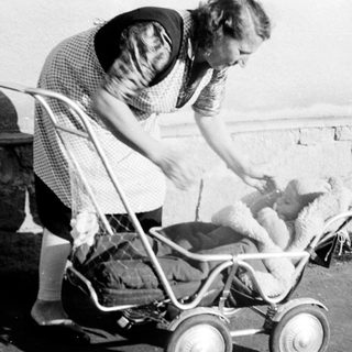 Woman tending to a baby in an old-fashioned stroller.