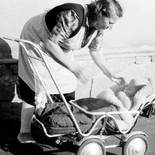 Woman tending to a baby in an old-fashioned stroller.