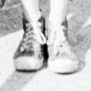 Boy in overalls stands on a bridge, looking at camera.