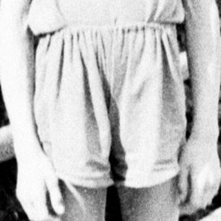 Boy in overalls stands on a bridge, looking at camera.