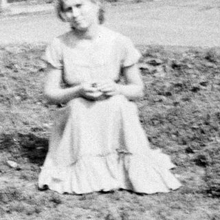 Young girl sits in a field, houses in background.