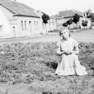 Young girl sits in a field, houses in background.