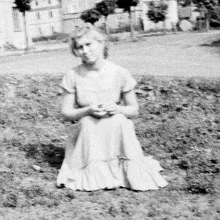 Young girl sits in a field, houses in background.