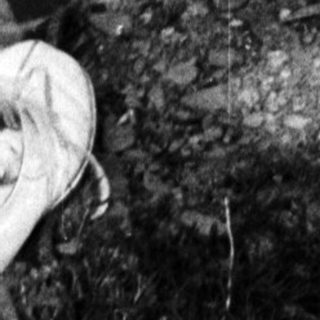 Here's a brief summary of the image: Bare-chested man sits on a rock, barefoot in nature.
