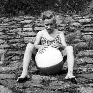 Girl sits on rocks, holding a ball.