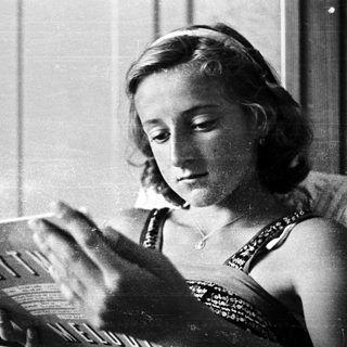 Here's a brief summary of the image: Woman reading a magazine while reclining on a bed.