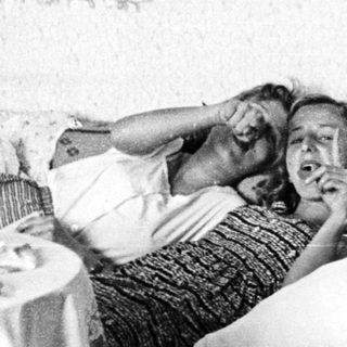 Here's a brief summary of the image: Woman lies in bed, appears to be listening intently.