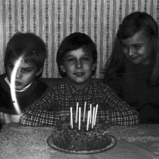Three children blow out candles on a cake.
