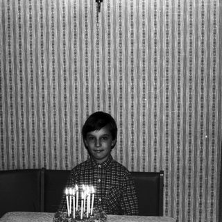 Boy sits at table with birthday cake and candles.