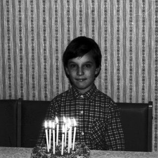Boy sits at table with birthday cake and candles.