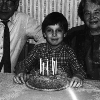 Boy with cake, flanked by grandparents in a vintage photo.