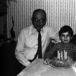 Boy with cake, flanked by grandparents in a vintage photo.