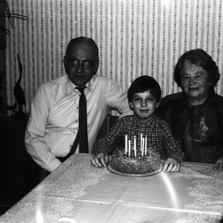 Boy with cake, flanked by grandparents in a vintage photo.