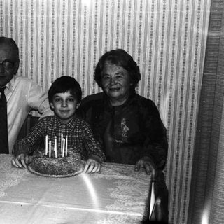 Boy with cake, flanked by grandparents in a vintage photo.