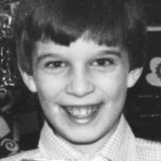 Boy smiles, holding a wrapped gift near a Christmas tree.