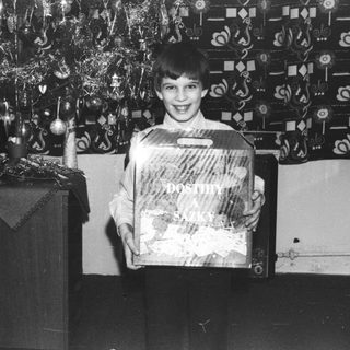 Boy smiles, holding a wrapped gift near a Christmas tree.