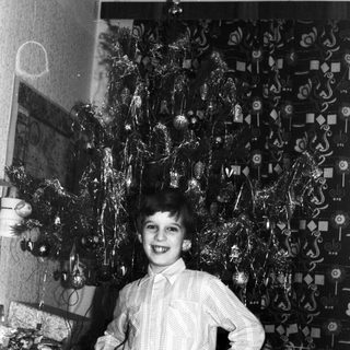 Boy stands proudly next to a decorated Christmas tree.