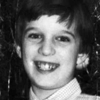 Boy stands proudly next to a decorated Christmas tree.
