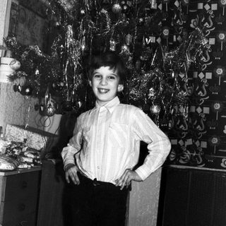 Boy stands proudly next to a decorated Christmas tree.
