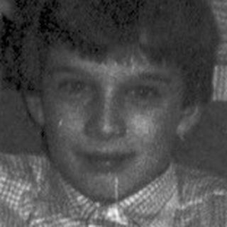 Boy sits on chair, facing camera, in a room.