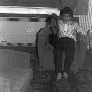 Boy sits on chair, facing camera, in a room.