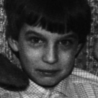Boy sits with stuffed animals in a sparsely furnished room.