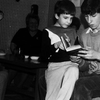 Two boys reading a book together at a table.